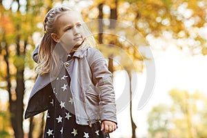 Fashionable little girl plays with autumn leaves. Happy child outdoors. Autumn kids fashion. Autumn holidays. Copy space.Beautiful