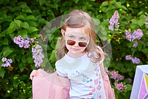 fashionable little girl in sunglasses walks through a blooming garden.