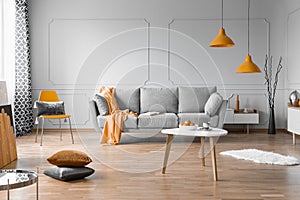 Fashionable living room interior design with grey couch, wooden coffee table and orange accents