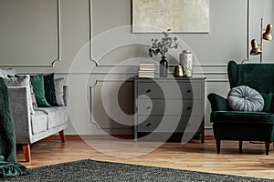 Fashionable living room interior with wooden commode, scandinavian sofa and emerald green armchair