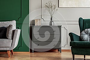 Fashionable living room interior with wooden commode, scandinavian sofa and emerald green armchair