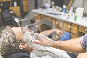 Fashionable man client during beard shaving in barber shop