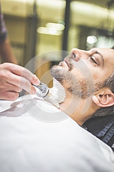 Fashionable man client during beard shaving in barber shop