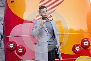 Fashionable man in a gray coat against the background of a red bus