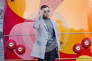 Fashionable man in a gray coat against the background of a red bus