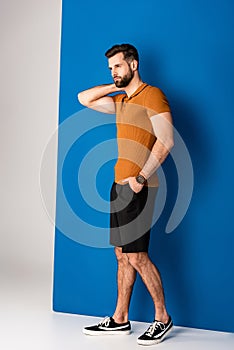 Fashionable man posing in shorts and brown polo on grey and blue