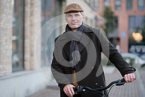 Fashionable man in woolen coat and Irish cap stands with his bicycle on a street