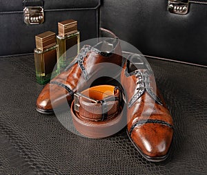 Fashionable men`s shoes of brown color with two bottles of men`s perfumes stand on a table covered with python skin