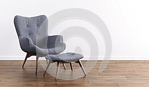 Fashionable modern gray armchair with wooden legs, ottoman against a white wall in the interior. Furniture, interior object,