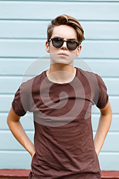 Fashionable modern young hipster man in dark sunglasses in trendy summer t-shirt with stylish hairstyle stands