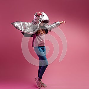 Fashionable and modern young woman in a puffy light down jacket throws a hood over her head.