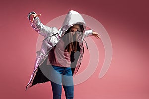 Fashionable and modern young woman in a puffy light down jacket throws a hood over her head.