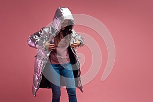 Fashionable and modern young woman in a puffy light down jacket throws a hood over her head.