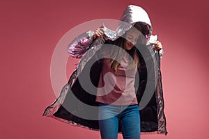 Fashionable and modern young woman in a puffy light down jacket throws a hood over her head.