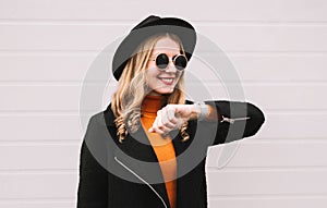 Fashionable portrait happy young smiling woman looking at smart watch using voice assistant or takes calling on city street