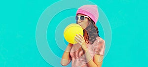 Fashionable portrait stylish cool young woman inflating chewing gum wearing pink hat on blue background