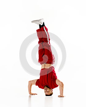 Fashionable portrait. Stylishly dressed man dancing breakdance, freestyle, standing on head at dancehall against white