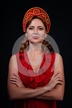 Fashionable portrait of woman wearing red dress and red kokoshnik with crossed arms . Isolated on black background.Studio shot