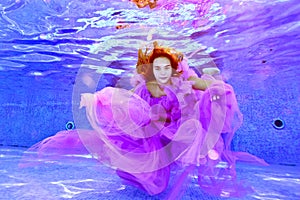 A fashionable portrait of a young girl in a beautiful purple dress, who poses for the camera under the water in an