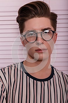 Fashionable portrait of a young handsome hipster man with piercing with a hairstyle in trendy glasses in a striped fashionable t-