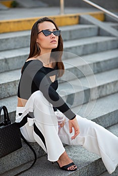Fashionable pretty stylish girl posing ouside. Street fashion. Beautiful young brunette woman wearing white trousers and black