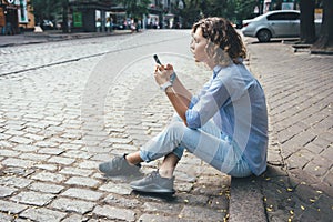 Fashionable relaxed young woman sitting on the sidewalk