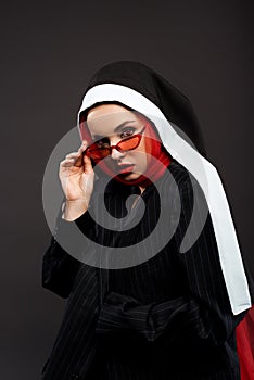 Fashionable sexy demoniac nun with red eyes posing in black suit, red sunglasses and scarf