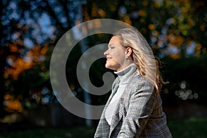 Fashionable smiling middle-aged woman with long wavy hair in checkered jacket and grey roll-neck sweater sit luxuriating