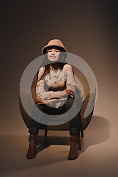fashionable smiling woman in hat sitting in armchair