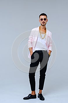 Fashionable sophisticated man in a pink jacket and black trousers, wears a gold chain, the expression of emotions gestures with