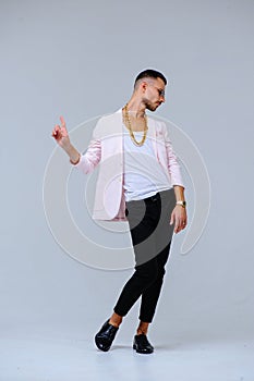 Fashionable sophisticated man in a pink jacket and black trousers, wears a gold chain, the expression of emotions gestures with