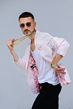 Fashionable sophisticated man in a pink jacket and black trousers, wears a gold chain, the expression of emotions gestures with