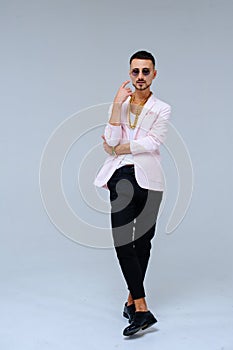 Fashionable sophisticated man in a pink jacket and black trousers, wears a gold chain, the expression of emotions gestures with