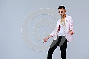 Fashionable sophisticated man in a pink jacket and black trousers, wears a gold chain, the manifestation of emotions gestures hand