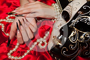 Fashionable stilettos nails design with Venetian buffoon mask, beads on red silk