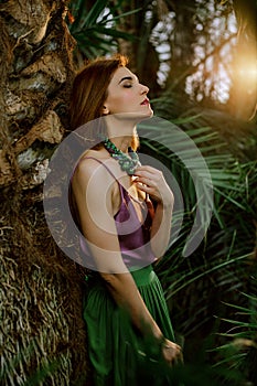 Fashionable style. Beauty with natural make-up in a tropical greenhouse. Beautiful female model in a casual dress, standing around