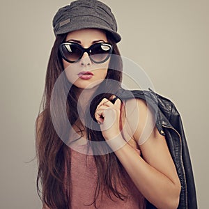 Fashionable style female model in fashion sunglasses posing holding the hand black leather jacket on blue background. Summer