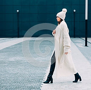 Fashionable stylish looker girl in white cap and knit coat. Walks on the street. Outdoor. Streetstyle.