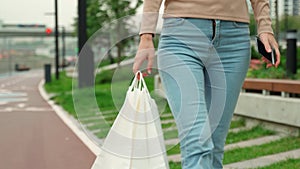 Fashionable stylish woman in blue jeans walking with a package along a busy street in a big city, buying clothes for