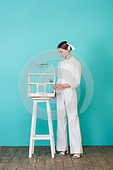 fashionable teen girl in stylish white outfit looking at parrot in cage