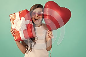 fashionable teen girl in sunglasses hold giftbox and heart balloon. love gift. surprised kid