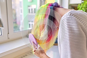 Fashionable teen girl with trendy rainbow dyed hair combing hair at home