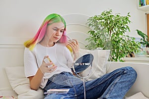 Fashionable teenage girl at home on bed with make-up mirror, holding brush and highlighter