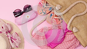 Fashionable trendy beach accessories for woman appear on pastel pink background. Stop motion flat lay summer concept