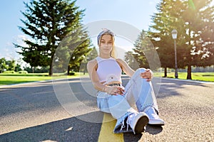 Fashionable trendy teenage hipster female sitting on road in park