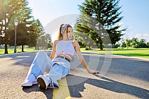 Fashionable trendy teenage hipster female sitting on road in park