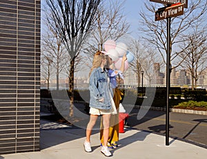 Fashionable urban girls wearing trendy outfit with balloons walking on New York City street.