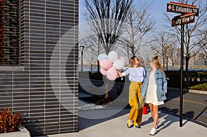 Fashionable urban girls wearing trendy outfit with balloons walking on New York City street.