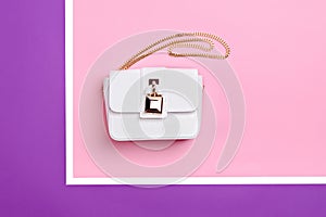 Fashionable white leather women\'s handbag with gold shoulder chain and stylish metal clasp on a multi-colored background