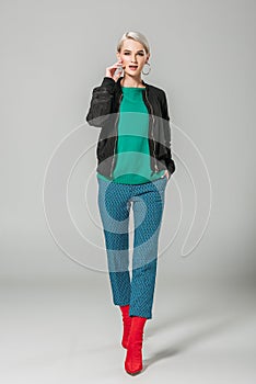 fashionable woman in black jacket and red boots posing on grey